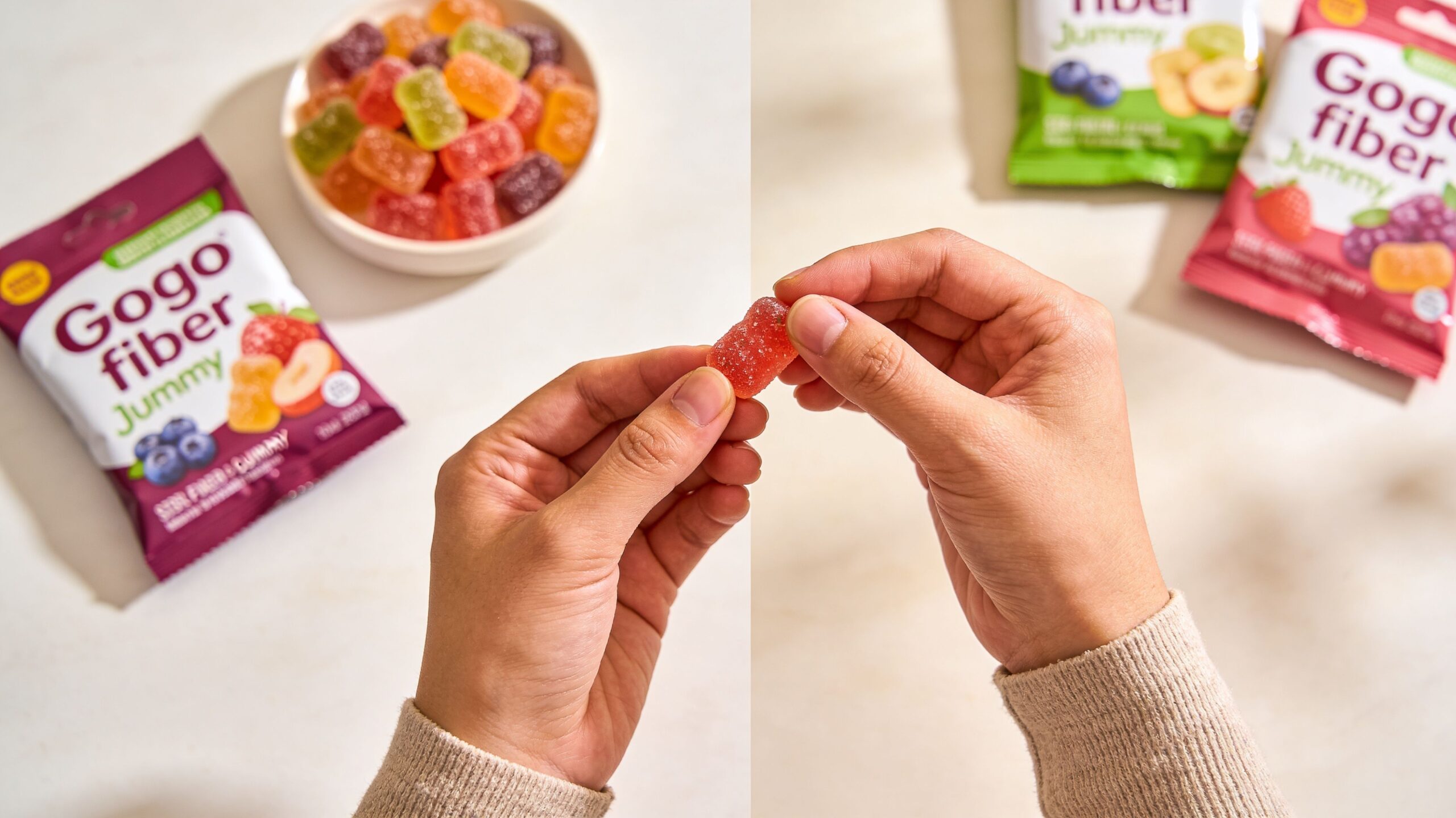 A pair of hands holds a red gummy candy next to Gogo fiber gummy product packaging.